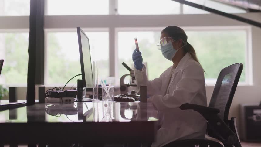 A scientist checks a test tube while sitting at her desk