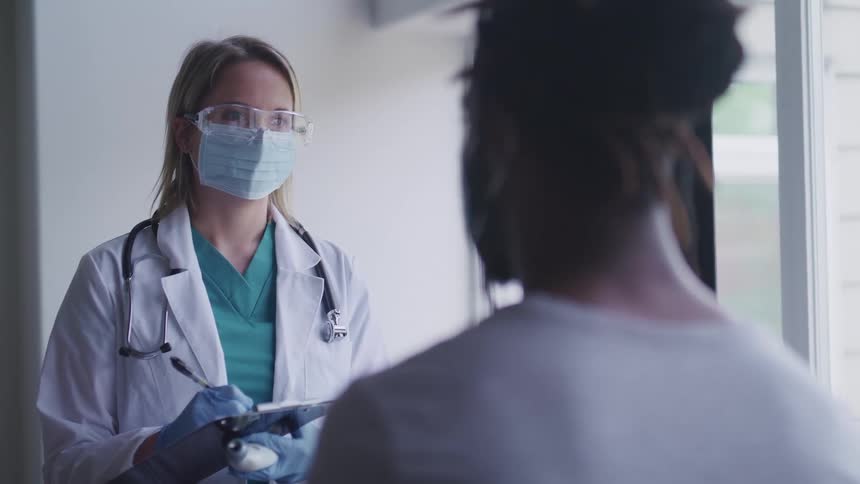 Female doctor wearing a mask writes as she speaks with a patient