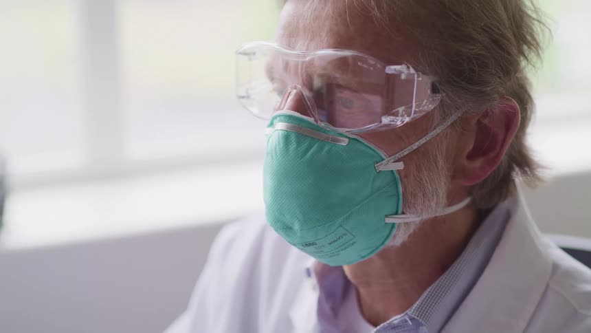 Doctor works near window while wearing medical mask and goggles