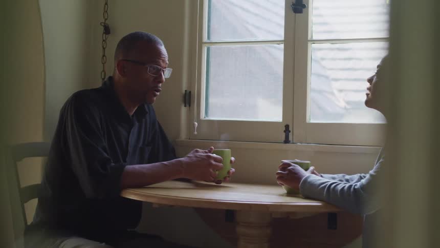 Couple sit at breakfast nook near window drinking coffee and talking