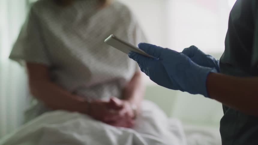 A nurse uses a tablet as she talks to a patient