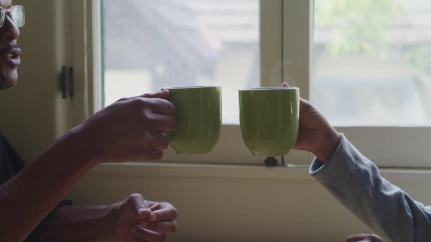 A man uses his coffee mug to cheers another person holding a mug