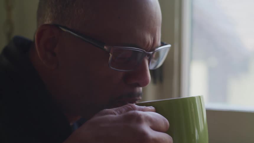 Middle aged black man with glasses drinks a green cup of coffee