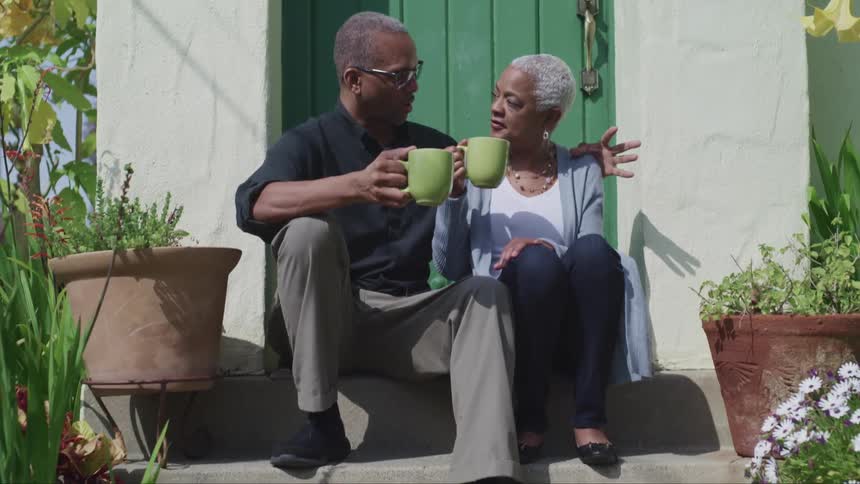 A man and woman chat while drinking coffee and cuddling on a front doorstep