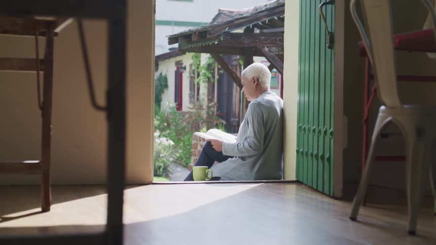 A woman sitting by a door entrance reading a book next to a mug