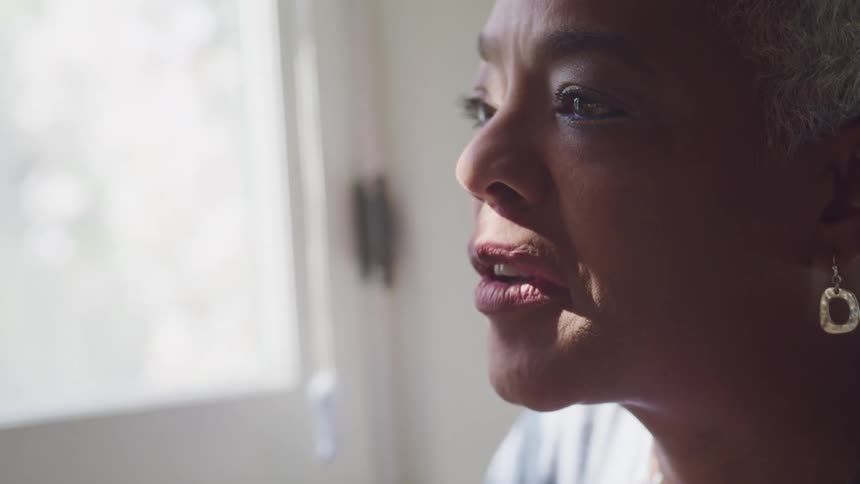 A black woman laughs and drinks coffee while sitting next to a window