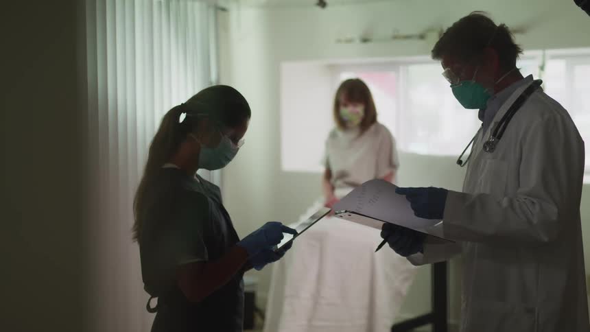 A patient sits on an exam table as a doctor and nurse talk and looks at charts