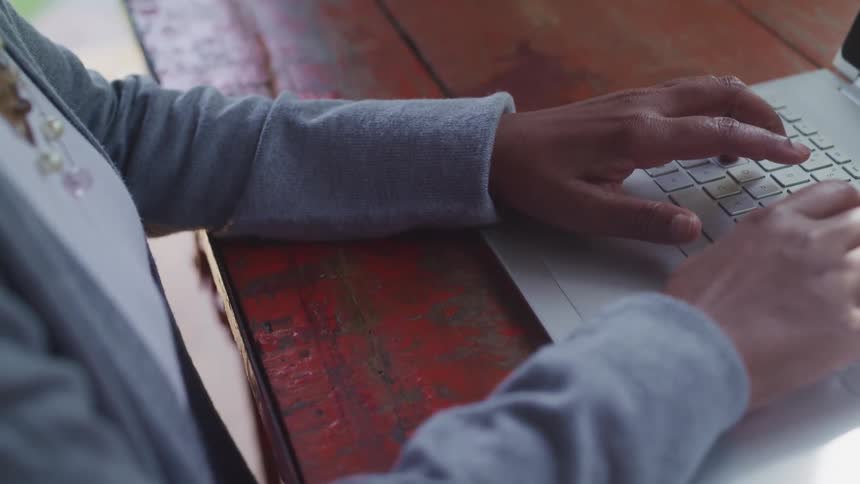 Woman types on a laptop keyboard that is sitting on a wooden table