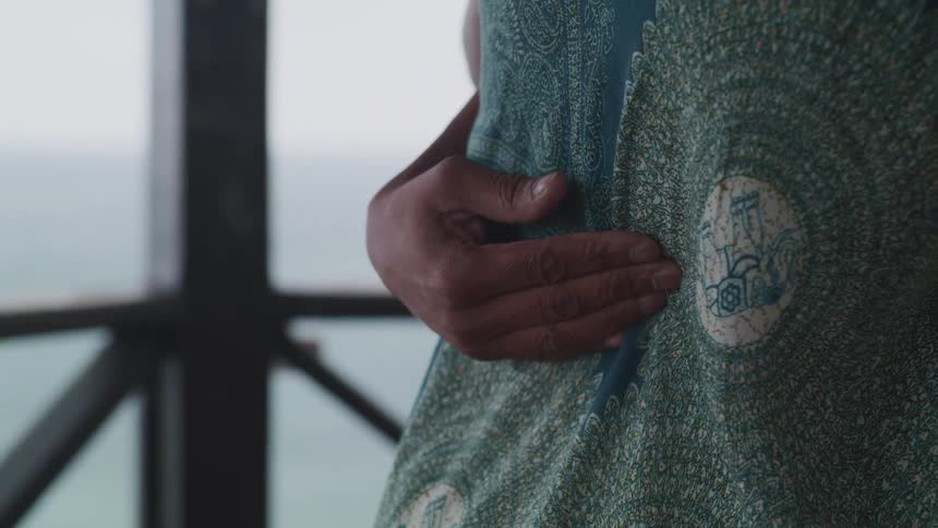 A woman with her hand on her stomach sways in front of a window