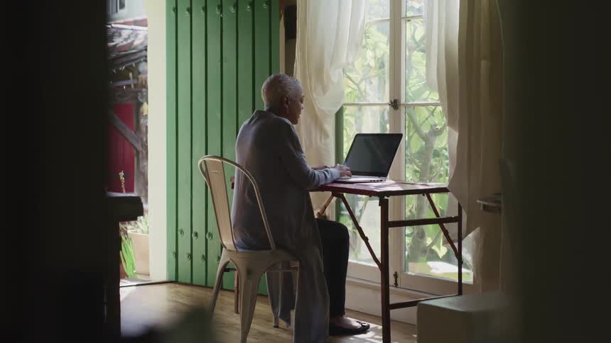 Black woman with short hair sits at a desk and uses a laptop in a room