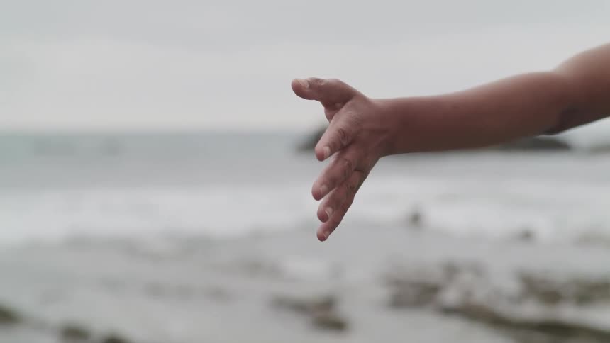 A woman stands with her arm outstretched on the beach