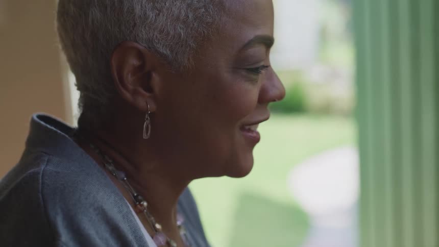 Woman wearing earrings and a necklace smiles while she is near a window