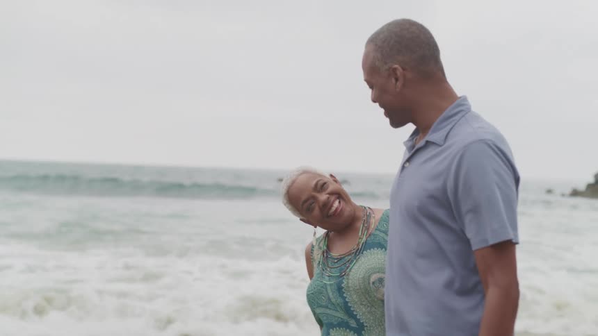 A man and woman walk down the beach holding hands and laughing
