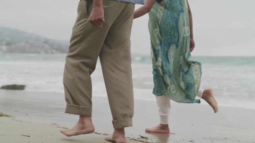 Couple holding hands walking barefoot on the shoreline at the beach