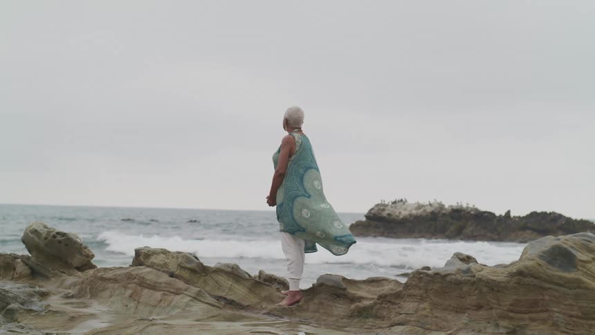 A woman is standing by the coast of an ocean