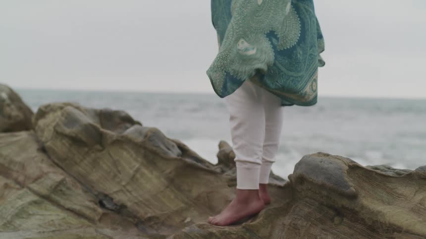 A woman standing on a rock with the ocean sky and clouds in the background