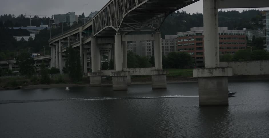 A boat floats under a large city bridge