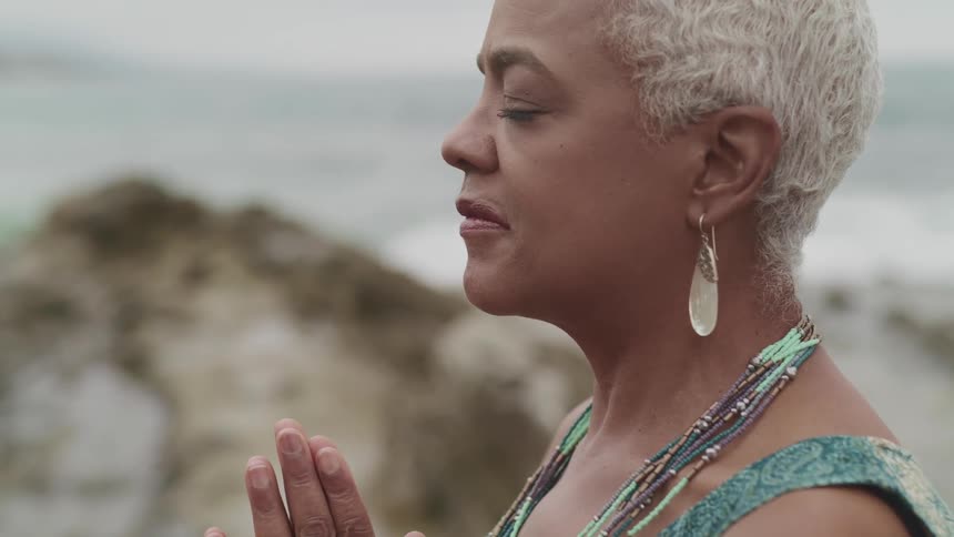 Woman with hands together praying on a cliffside near the beach