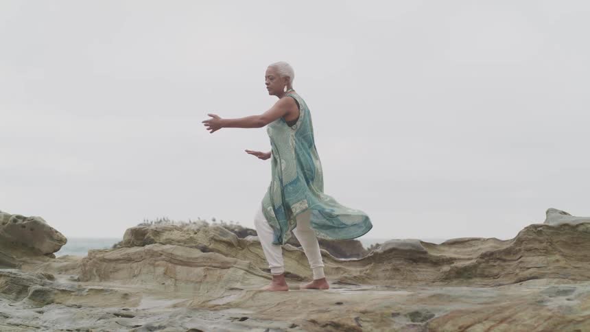 An older woman stands on sandstone terrain as she practices various poses