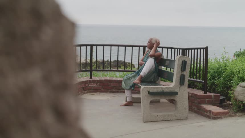 A woman sits quietly on a bench above the ocean