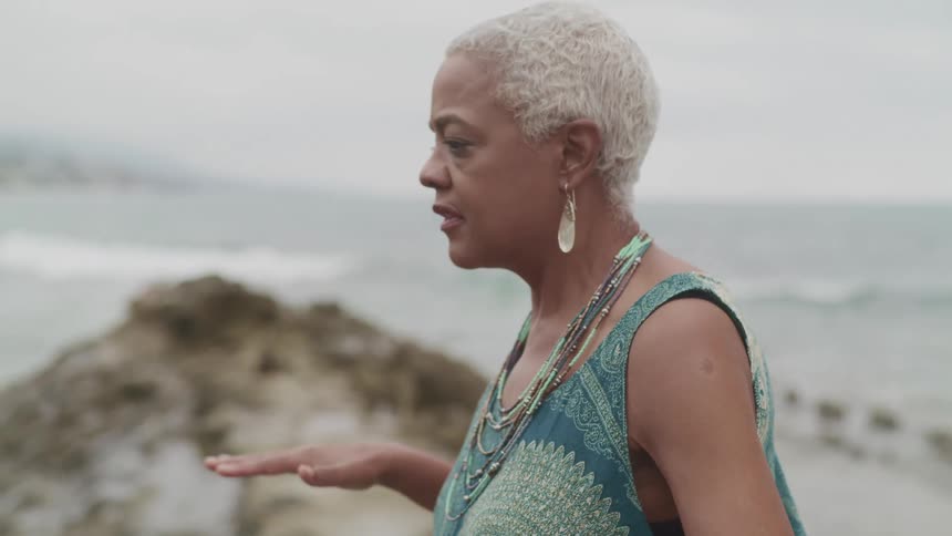 Older woman meditating top of a cliff overlooking the coast