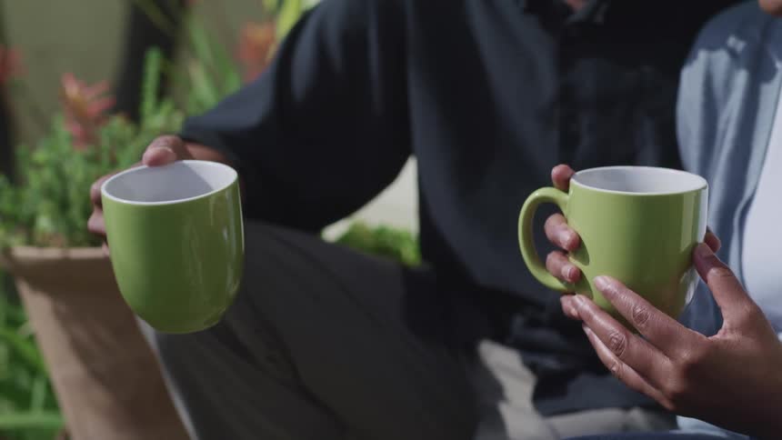 A man and woman sit outside together holding coffee cups