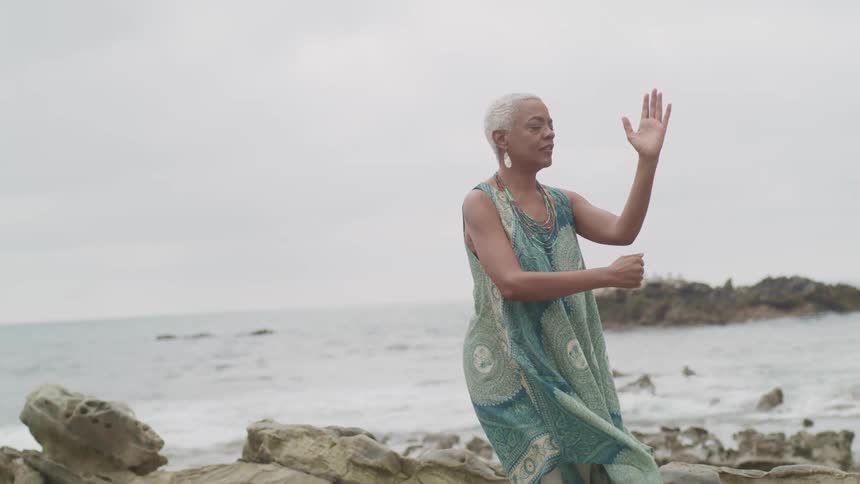A woman doing yoga on a rock formation next to the ocean on a cloudy day