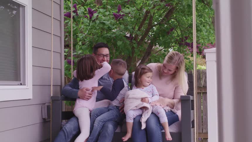 A man and a woman hold children on their laps as they sit on a porch swing outside of a house