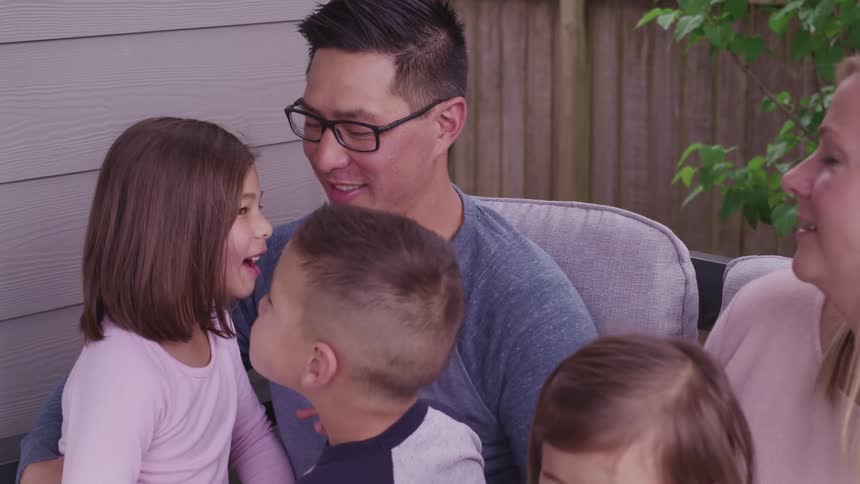 Family sits on porch swing smiling and talking