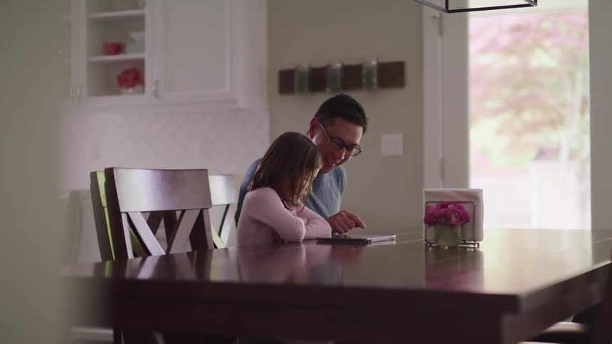 A father and daughter use a tablet in the dining room