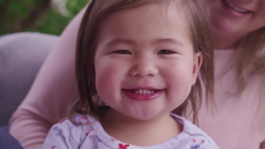 Close up of a smiling girl looking at the camera sitting on a womans lap