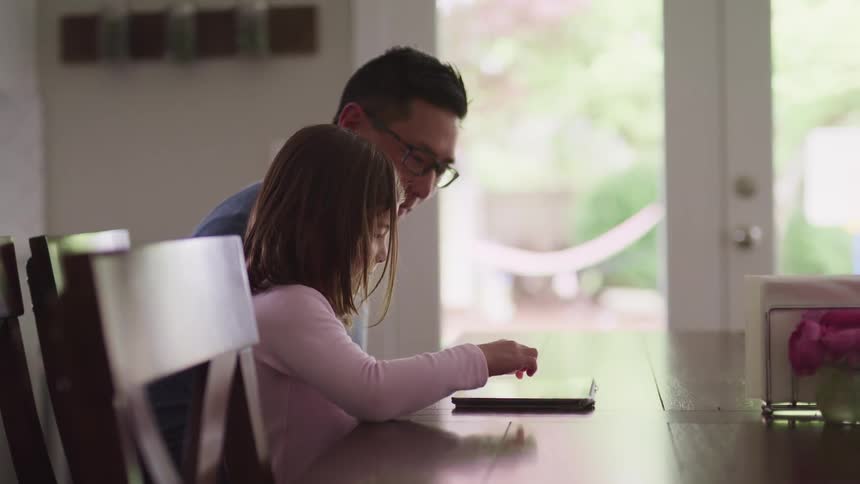 A father and daughter use a tablet at the table