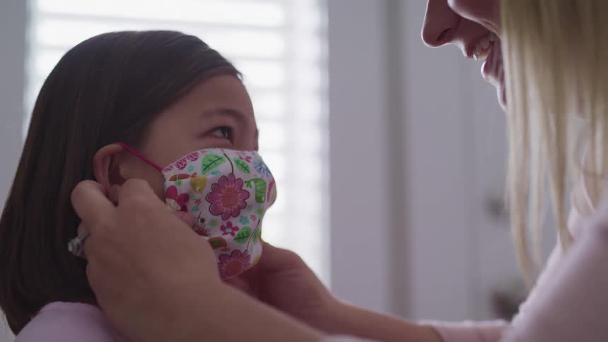 A woman places a face mask on a girl