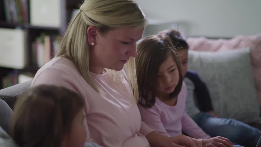 Blond woman sits on a sofa with three young children