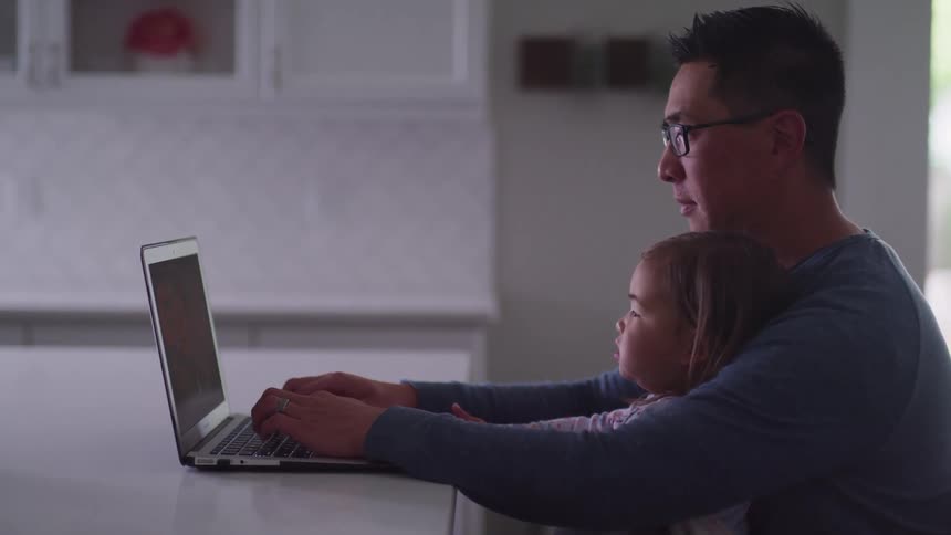 A little girl sits on her dads lap and they look at a laptop
