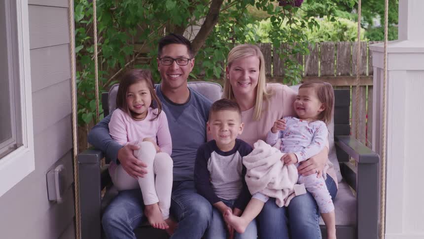A family of five smile as they pose for a portrait on a bench on their front porch