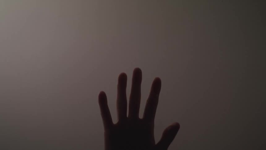 Silhouette of a hand sliding down a glass pane