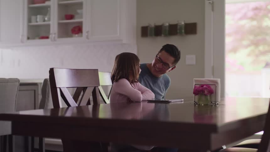 A father smiles at his daughter as they sit at their kitchen table