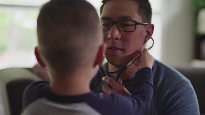 Son standing in front of father places a stethoscope into his fathers ears