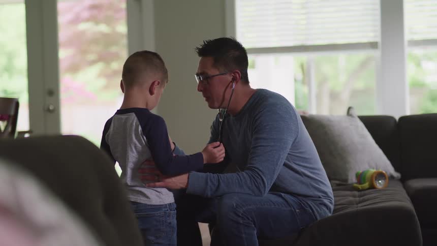 Man checks child with stethoscope while sitting on couch in house