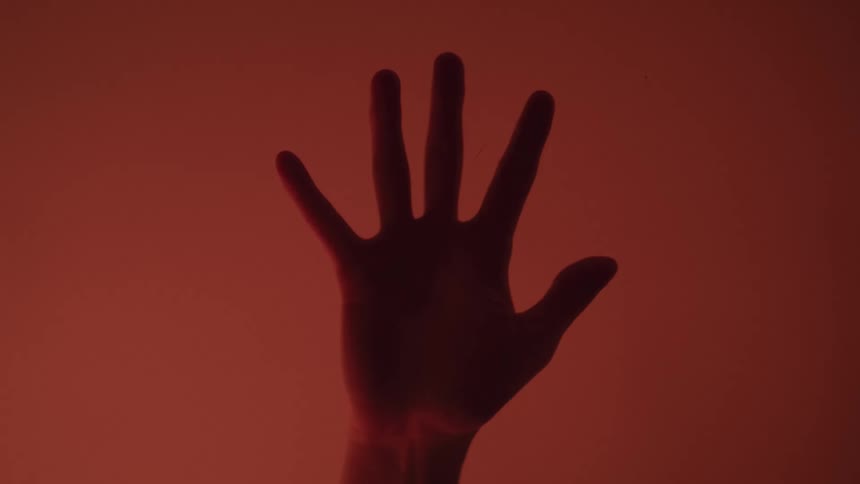 Hand reaches upward fingers spread tinted red against red background