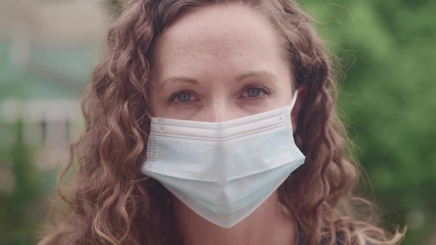 Woman with brown curly hair and a white face mask