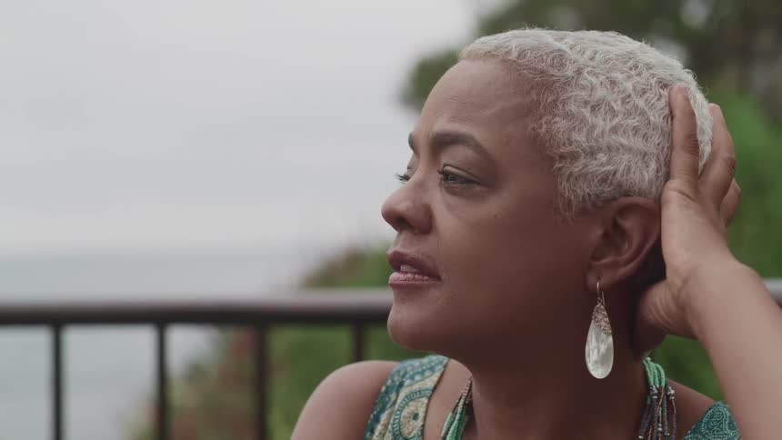 A shorthaired black woman relaxes outdoors at oceanside on a cloudy day