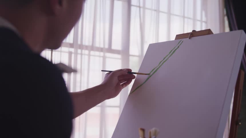 A person stands in front of a canvas and uses a paintbrush to paint a line
