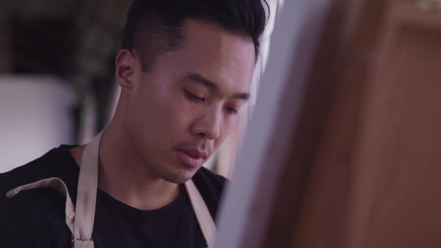 A man with a apron in front of a canvas next to a window