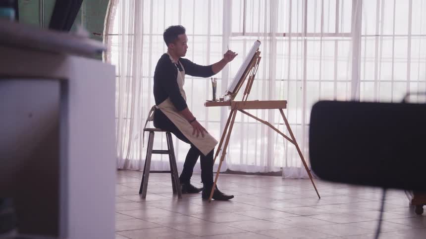 A man is painting indoors on an easel