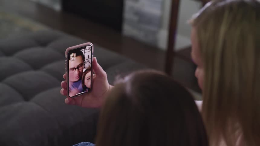 A woman and her daughter use a smartphone to wave at a man and his daughter over video chat