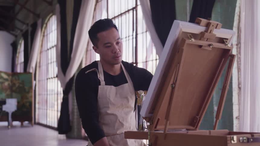 A man is painting on an easel indoors