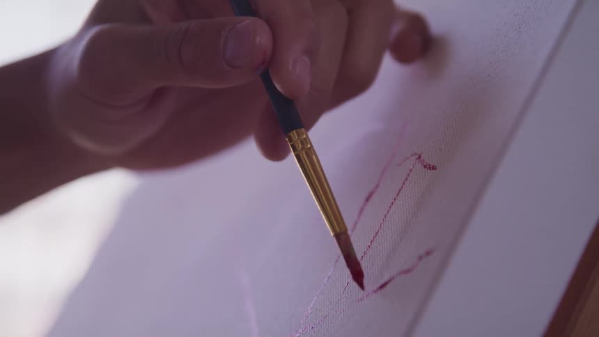 A painter uses a small paintbrush to draw on a piece of paper