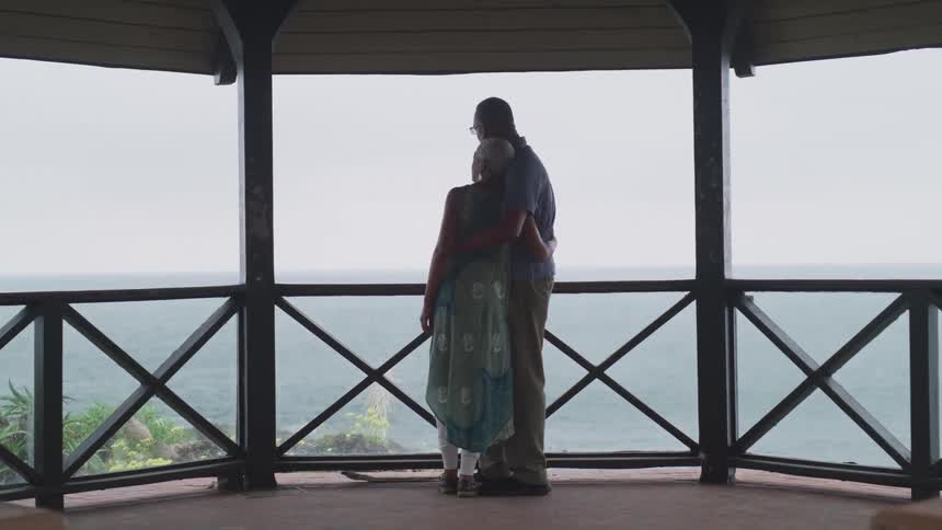 A husband and wife embrace as they stand on a gazebo overlooking the ocean